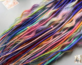 May include: A collection of colorful dreadlocks in shades of blue, pink, orange, green, and purple. The dreadlocks are arranged in a diagonal pattern, with some strands having small beads. The image is taken from a top-down perspective.