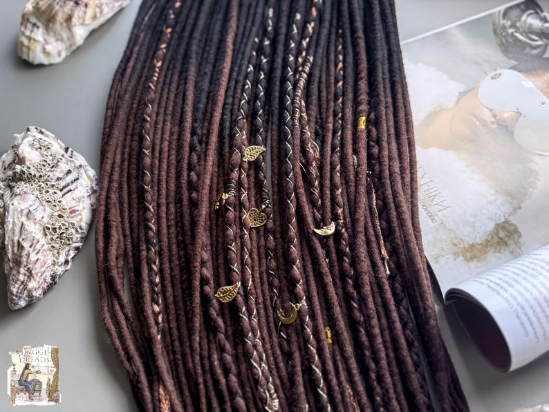 a collection of brown braided hair accessories, including beads and charms, arranged on a surface alongside a magazine or book.