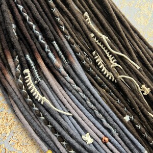 May include: A set of brown and gray synthetic dreadlocks with white and black stitching and beads. The dreadlocks are ombre, with the brown fading to gray.