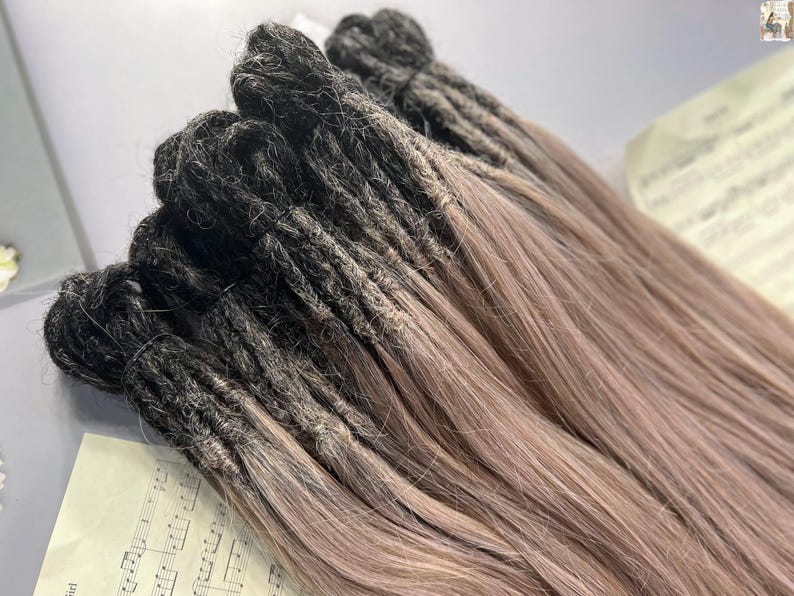 May include: A bundle of dreadlocks with a color gradient. The roots are dark, transitioning to a light brown at the ends. The dreadlocks are neatly bundled together, suggesting they are extensions or a hair accessory.