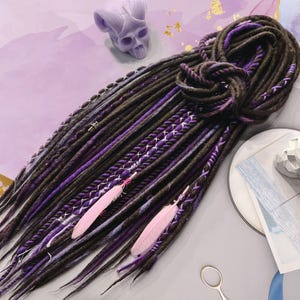 May include: A set of brown and purple synthetic dreadlocks with pink feathers. The dreadlocks are tied together at the top.