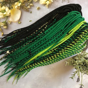 May include: A set of synthetic dreadlocks in black, green, and yellow. The dreadlocks are arranged in a fan shape and have beads and gold thread accents.