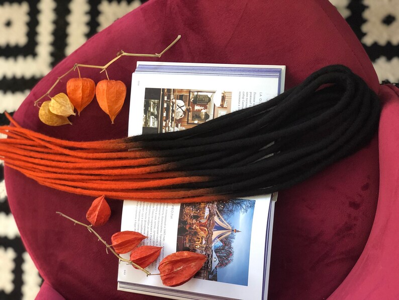 May include: A set of ombre dreadlocks with a black to orange colour gradient. The dreadlocks are made of synthetic hair and are approximately 24 inches long.