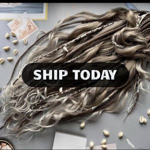 Peut inclure: Un ensemble d'extensions capillaires synthétiques composé de mèches ondulées et lisses dans des tons marron, blond et gris. Les cheveux sont ornés de fils blancs enroulés et de petits coquillages. Un encart noir affiche le texte SHIP TODAY.