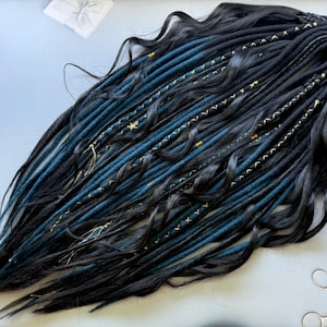 May include: Black and blue dreadlocks with gold accents. The synthetic hair extensions are arranged in a wavy pattern. The dreadlocks are decorated with gold stars and other small gold embellishments.