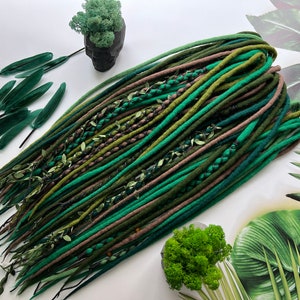 May include: Green, brown, and black synthetic dreadlocks with green leaves woven in. The dreadlocks are arranged in a pile on a white surface.