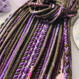 May include: A set of brown and purple synthetic dreadlocks with pink and white accents. The dreadlocks are made of a soft, textured yarn and are perfect for adding a touch of color and style to your hair.
