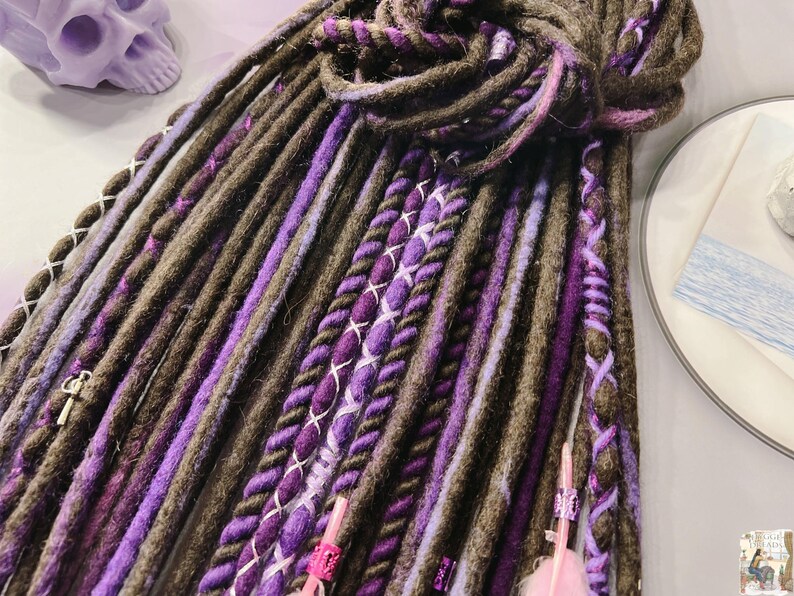 May include: A set of brown and purple synthetic dreadlocks with pink and white accents. The dreadlocks are made of a soft, textured yarn and are perfect for adding a touch of color and style to your hair.