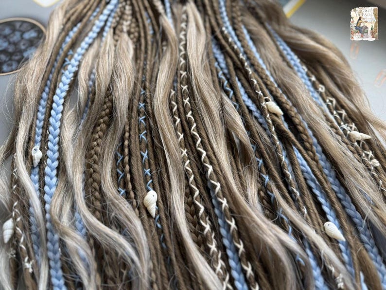 a close-up view of a collection of braided hair strands in various shades of brown and blonde, with small white shells or beads interspersed throughout the braids.