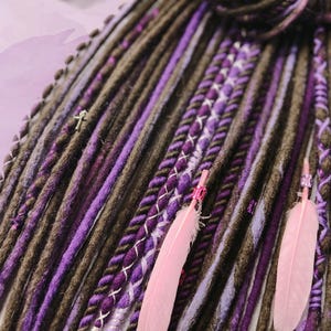 May include: A set of brown and purple synthetic dreadlocks with pink feathers and silver beads. The dreadlocks are made of a soft, textured yarn and are perfect for adding a touch of bohemian style to any look.