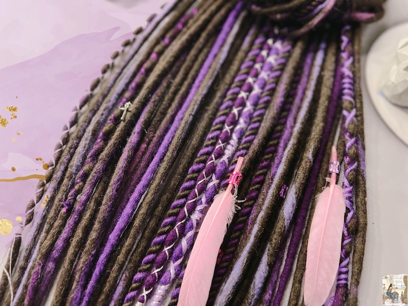 May include: A set of brown and purple synthetic dreadlocks with pink feathers and silver beads. The dreadlocks are made of a soft, textured yarn and are perfect for adding a touch of bohemian style to any look.