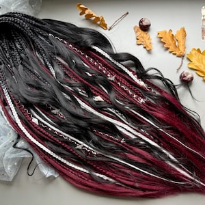 Puede incluir: Dreadlocks negros y burdeos con detalles blancos y burdeos. Los dreadlocks están decorados con pequeños abalorios plateados. La imagen también incluye hojas de otoño y una pequeña ilustración.