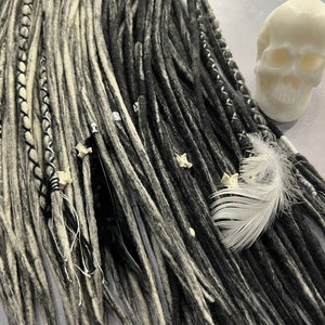 Puede incluir: Dreadlocks sintéticas negras y blancas con una pluma blanca y una calavera blanca.