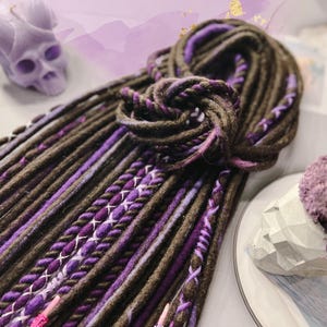 May include: A bundle of brown and purple synthetic dreadlocks. The dreadlocks are tied together in a knot.