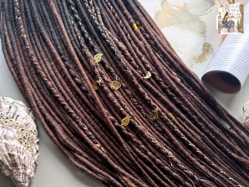 a collection of long, brown braided hair strands arranged on a surface, with some of the braids adorned with small gold or silver charms.
