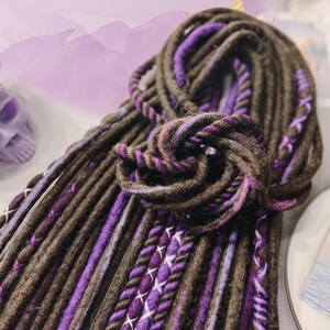 May include: A bundle of brown and purple synthetic dreadlocks. The dreadlocks are made of a soft, textured yarn and are ready to be added to your hair.