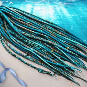 Könnte beinhalten: Ein Satz blauer und brauner synthetischer Dreadlocks mit goldenen Perlen. Die Dreadlocks sind fächerförmig auf einer hellgrauen Oberfläche angeordnet.