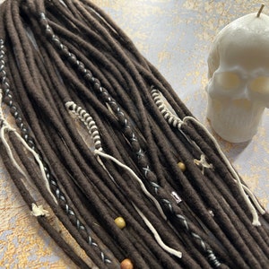 May include: Brown synthetic dreadlocks with white and silver accents. The dreadlocks are decorated with beads and other embellishments.