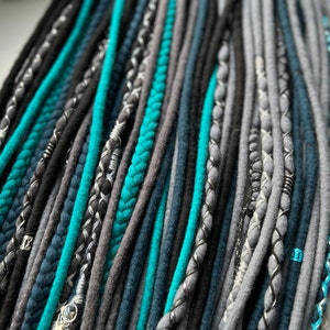 Puede incluir: Una colección de rastas sintéticas en tonos de turquesa, gris y negro. Las rastas están hechas de un material suave y peludo y tienen una variedad de texturas.