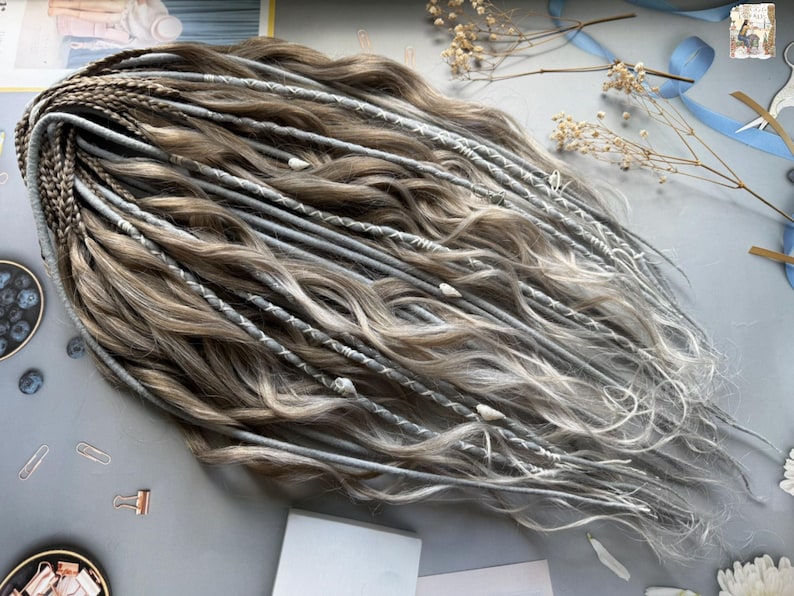 May include: A collection of handmade dreadlocks in shades of brown and gray, with some strands featuring white accents. The dreadlocks are styled with a wavy texture and adorned with decorative elements. A stylish hair accessory.
