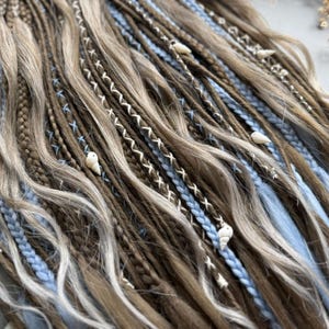 a close-up view of a collection of braided hair strands in various shades of brown and blonde, with some blue and white accents.