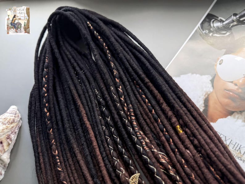 a collection of long, dark brown braided hair strands arranged on a surface, with a magazine featuring a woman's face in the background.