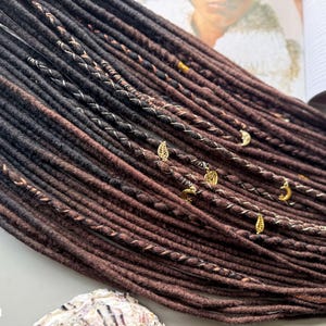 A close-up view of a collection of braided hair strands in various shades of brown, with small gold-colored accessories attached to some of the braids.