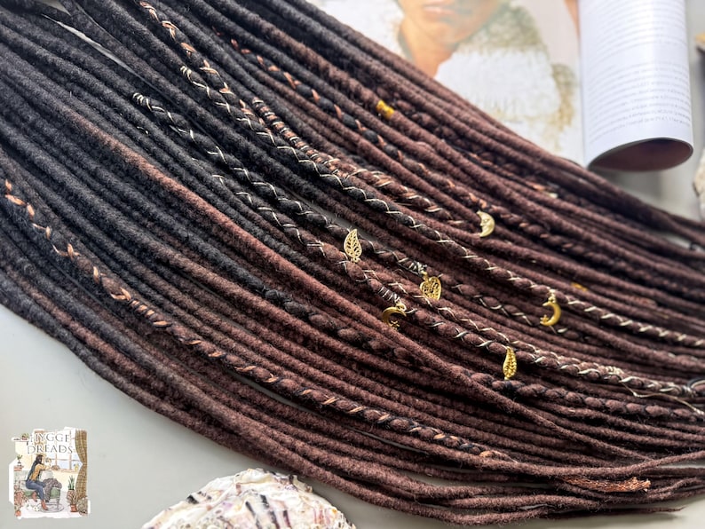 A close-up view of a collection of braided hair strands in various shades of brown, with small gold-colored accessories attached to some of the braids.