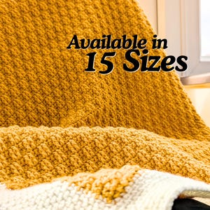 May include: A mustard yellow knitted blanket with a textured waffle stitch pattern. The fabric features a folded edge revealing a cream-colored underside. The text "Available in 15 Sizes" is printed in black over the center of the blanket.
