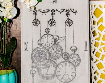 May include: A white wooden clock with a black and white design of gears and keys. The clock face has Roman numerals and the numbers VI, IX, XII, and III are visible. The clock is on a black stand.