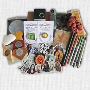 May include: A collection of themed merchandise featuring items like stickers, pins, and small books. The items have a fantasy theme, with references to "The Inkwood Hollow Collection" and "LOTR". There are also pens, a scrunchie, and a wooden leaf.