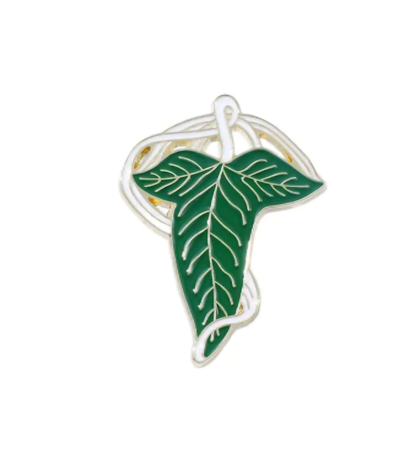 May include: A green leaf-shaped enamel pin with white veins and a silver-colored border. The pin features a stylized leaf design with a swirling, decorative element above the leaf. The pin is set against a white background.