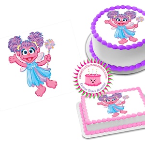 May include: An image of a round and rectangular cake decorated with a cartoon character. The cakes feature a white base with pink and purple frosting. The character is a pink fairy with blue clothing and a magic wand.