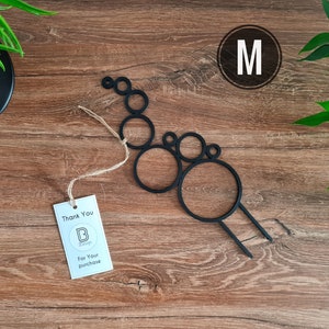 May include: Black metal wall decor shaped like a series of connected circles, with the letter "M" in a circle in the top right corner. The decor is on a wooden background.