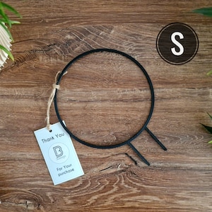 Op de afbeelding: Een zwarte metalen plantenstandaard met een ronde bovenkant en twee poten. De standaard staat op een houten oppervlak. De tekst "Thank You" en "For Your Purchase" staat op een wit label.