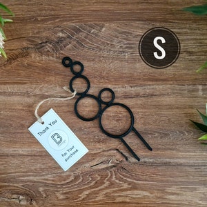 Könnte beinhalten: Schwarzer Pflanzenständer aus Metall mit einer Reihe verbundener Kreise. Der Ständer steht auf einer Holzoberfläche. Der Text "Thank You" und "For Your Purchase" befindet sich auf einem weißen Etikett.