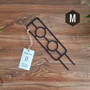 Könnte beinhalten: Schwarzer Pflanzenständer aus Metall mit zwei runden Öffnungen. Der Ständer steht auf einer Holzoberfläche. Der Text "Thank You" und "For Your Purchase" befindet sich auf einem weißen Etikett.