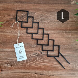 May include: Black metal wall decor with a geometric design. The decor is shaped like a staircase with six square frames. The decor is hanging on a wooden surface.