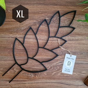 Könnte beinhalten: Schwarze Wanddekoration aus Metall in Form eines großen Blattes mit einem Dankeschön-Etikett, auf dem "Vielen Dank für Ihren Kauf" steht.