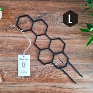 May include: Black metal hexagonal plant stand with two long spikes. The stand is on a wooden surface with a small thank you tag and a plant in a pot.