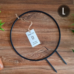 Può includere: Un cerchio di metallo nero con due steli di metallo che si estendono dal basso. Il cerchio è su una superficie di legno con un piccolo cartellino di ringraziamento che dice "Grazie per il tuo acquisto".