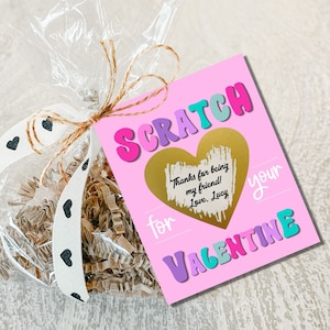 May include: Pink card with the words "SCRATCH for your VALENTINE" in colorful letters. A gold heart with the text "Thanks for being my friend! Love, Lucy" is in the center of the card.