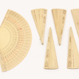 May include: A set of eight wooden folding fans with intricate cut-out designs. The fans are all closed and arranged in a row on a white background.