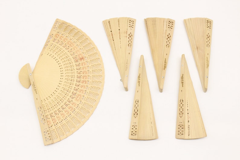 May include: A set of eight wooden folding fans with intricate cut-out designs. The fans are all closed and arranged in a row on a white background.