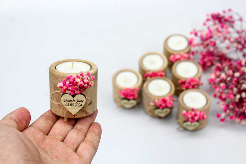 May include: Set of small wooden candle holders with a heart-shaped tag that says "Dean & Julie 08.08.2024" and pink dried flowers.