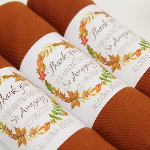 May include: Three brown scarves with white labels that say "Thank you for making this day so amazing" with a watercolor wreath of fall leaves and the date "02/06/2021" and the names "Allison & Jordan".