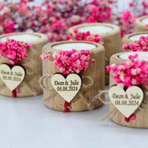 May include: Wooden candle holders with a small bouquet of pink flowers and a heart-shaped tag with the text "Dean & Julie 08.08.2024" on each.