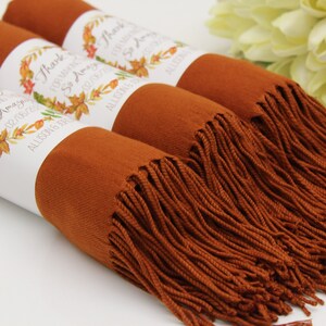 May include: Three rust-colored scarves with white labels that say "Thank you for making our day so amazing!" with a fall-themed wreath design. The labels also include the date "02/18/2017" and the names "Allison & Eric".