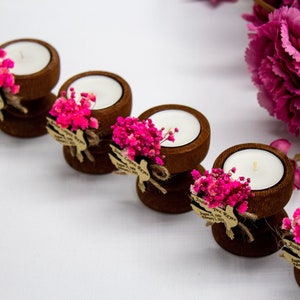 May include: Set of six small wooden candle holders with tea lights, each decorated with pink dried flowers and a small tag with the text "Jamie & Jose Reyes" and the date "August 11, 2023".
