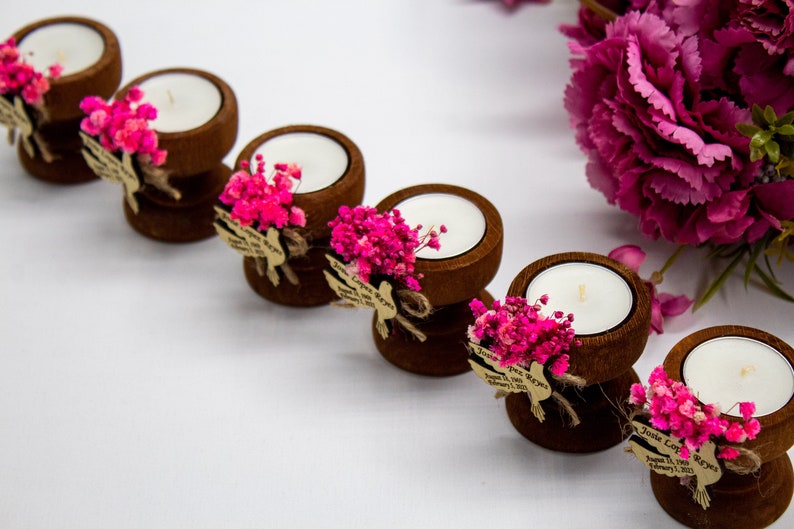 May include: Set of six small wooden candle holders with tea lights, each decorated with pink dried flowers and a small tag with the text "Jamie & Jose Reyes" and the date "August 11, 2023".
